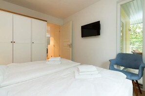 A hotel room with two beds, a TV mounted on the wall, and a chair.