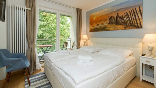 A bedroom with a large bed, a chair, a table, and a painting on the wall. - Villa Barbara, App. 09 (Heringsdorf)