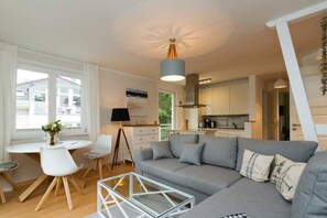 Un salon moderne avec un canapé gris, une table basse en verre et un coin repas comprenant des chaises blanches et une petite table.
