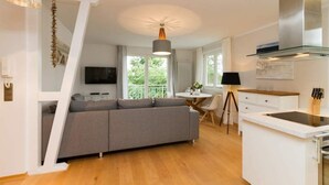 A modern kitchen with a grey sofa, a dining table, and a TV mounted on the wall. - Villa Barbara, App. 09 (Heringsdorf)