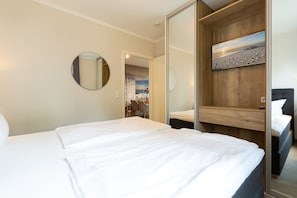 Een hotelkamer met een groot bed, een ronde spiegel, een houten hoofdbord en een schilderij van een strandlandschap.