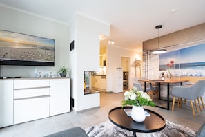 Een moderne woonkamer met een flatscreen-tv, een eethoek met een houten tafel en stoelen, en een keuken op de achtergrond.