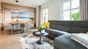 A modern living room with a grey sofa, a round coffee table, and a dining area with a wooden table and chairs. - Ostseedomizil Bansin, App. 1.1 (Heringsdorf)