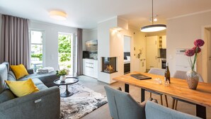 A modern living room with a sofa, a coffee table, and a dining area with a wooden table and chairs. - Ostseedomizil Bansin, App. 1.1 (Heringsdorf)