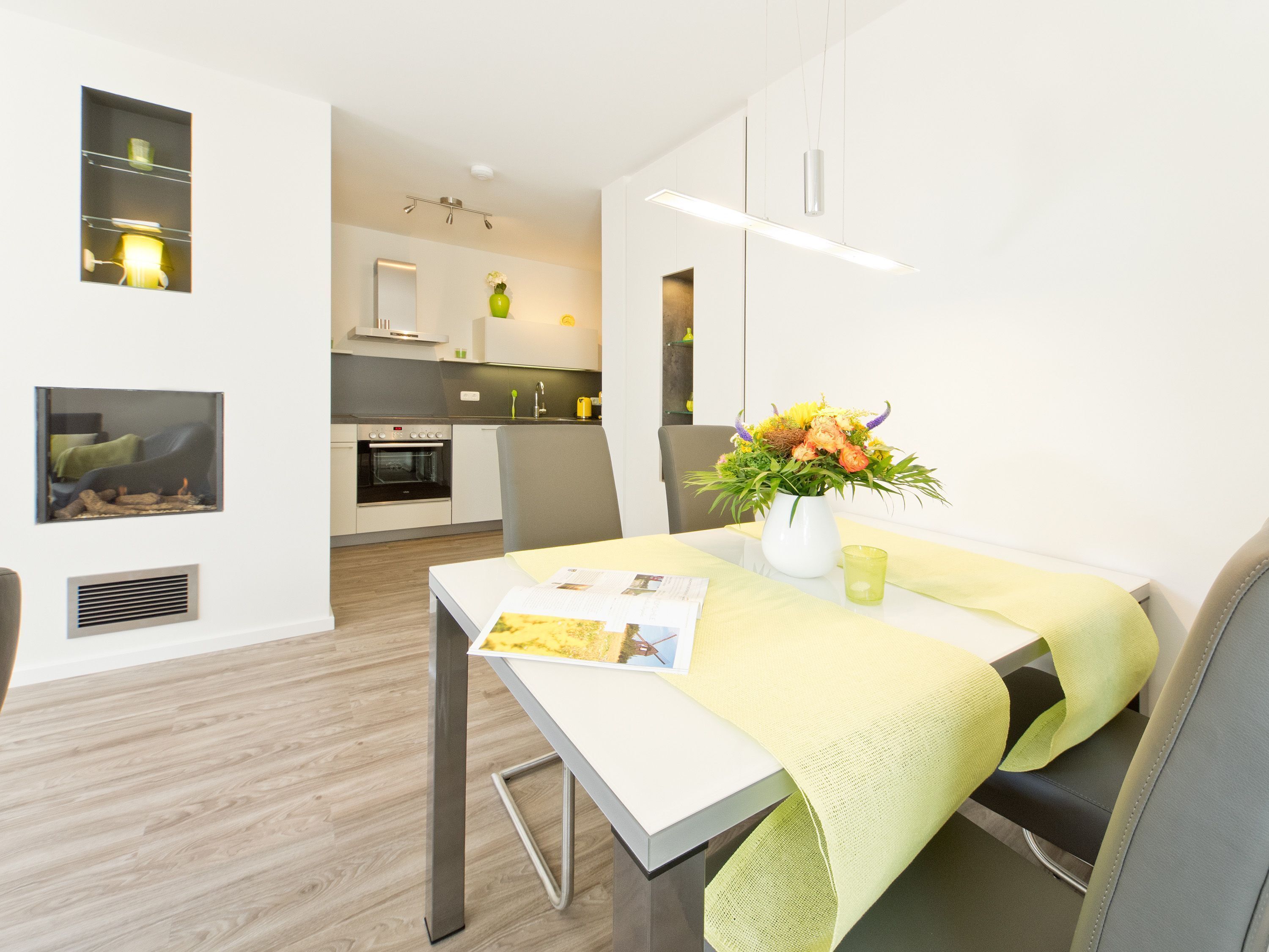Een moderne keuken met witte kastjes, een ingebouwde oven en een eethoek met een tafel en stoelen.