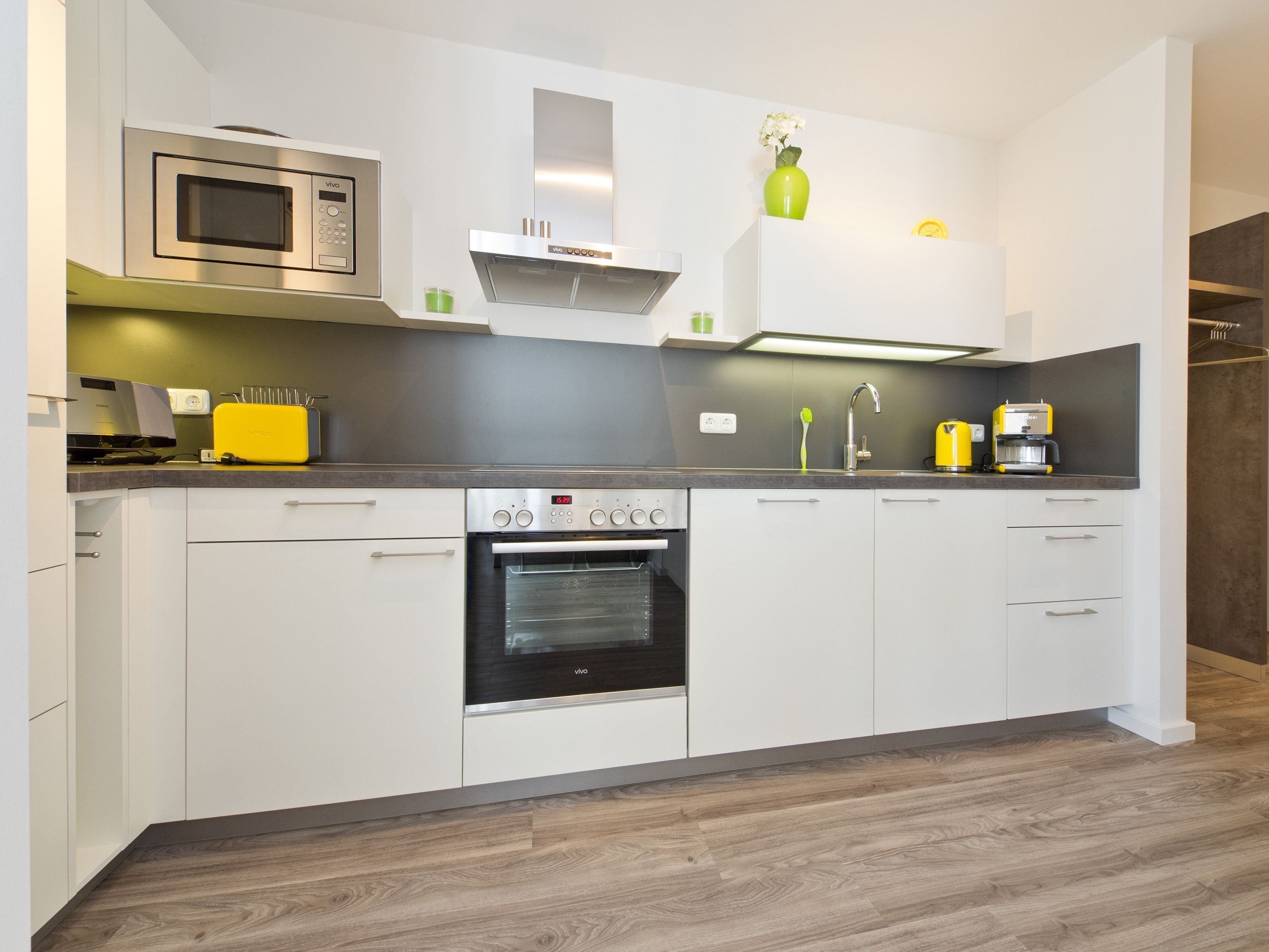 A modern kitchen with white cabinets, a microwave, a stove, and a coffee maker.