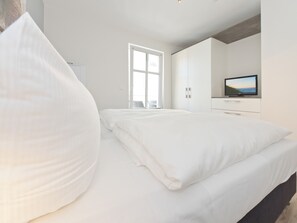 Ein modernes Schlafzimmer mit einem großen Bett, einem Fernseher und Blick ins Freie durch ein Fenster.