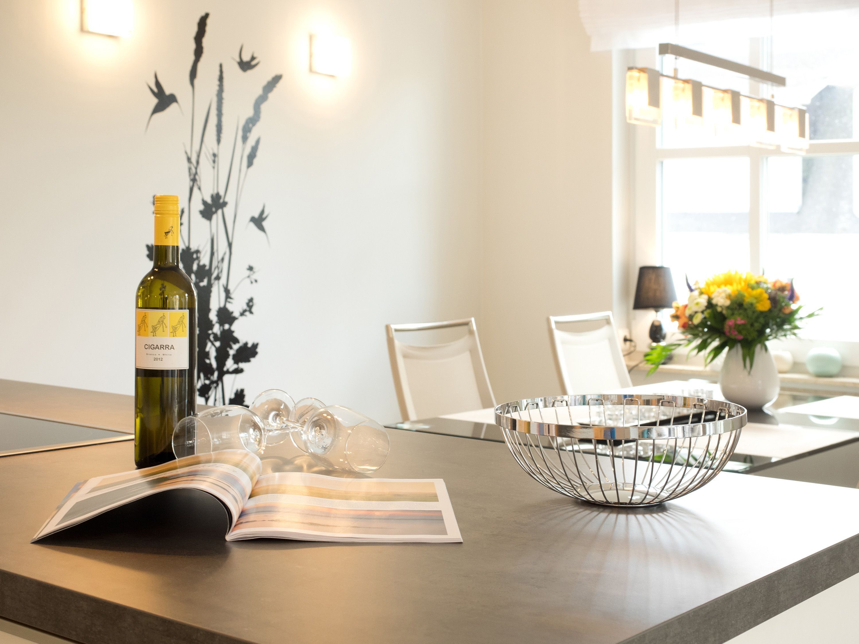 A modern dining area with a wine bottle, glasses, a magazine, and a decorative bowl on a table.