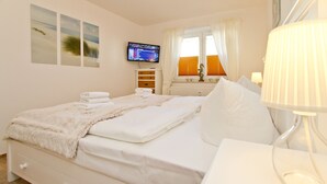 A hotel room with a bed, a TV on the wall, a window with curtains, and a lamp on the bedside table. - Apartment house Neuer Weg, App. 02 (Heringsdorf)