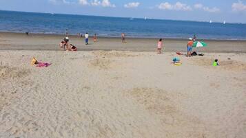 Una spiaggia con persone e barche sullo sfondo.