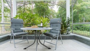 An outdoor patio with two grey cushioned chairs and a round table, surrounded by a metal railing and greenery. - Villa Marfa, App. 02 (Heringsdorf)