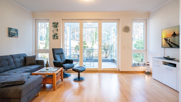 A spacious living room with a sofa, a chair, a coffee table, and a view through large sliding glass doors to an outdoor patio. - Villa Marfa, App. 02 (Heringsdorf)