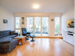 Amplia sala de estar con sofá, una silla, una mesa de centro y vistas a un patio exterior a través de grandes puertas corredizas de vidrio.