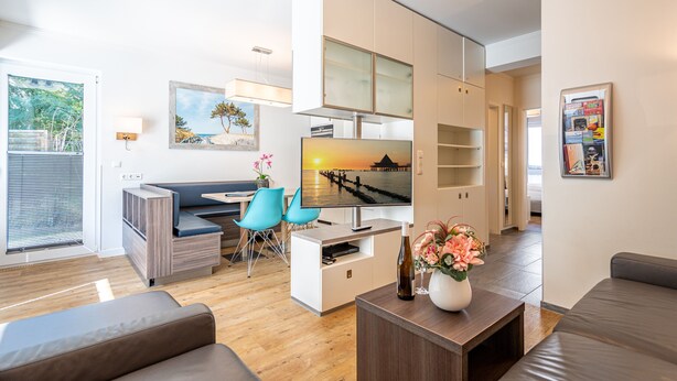 A modern living room with a flat-screen TV, a sofa, a coffee table, and a dining area with chairs. - Villa Limora, App. 02 (Heringsdorf)