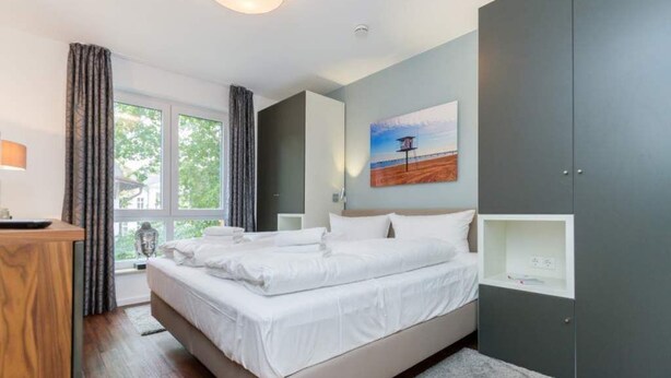 A modern bedroom with a large bed, bedside tables, a desk, and a window with curtains. - Villa Limora, apt. 04 (Heringsdorf)