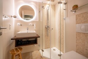 Un baño moderno con cabina de ducha de vidrio, tocador con lavabo y un taburete de madera.