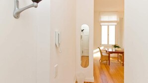 Un couloir avec un mur blanc, une porte dotée d’une poignée noire, une prise électrique blanche et un miroir qui reflète un coin repas avec une table et des chaises.