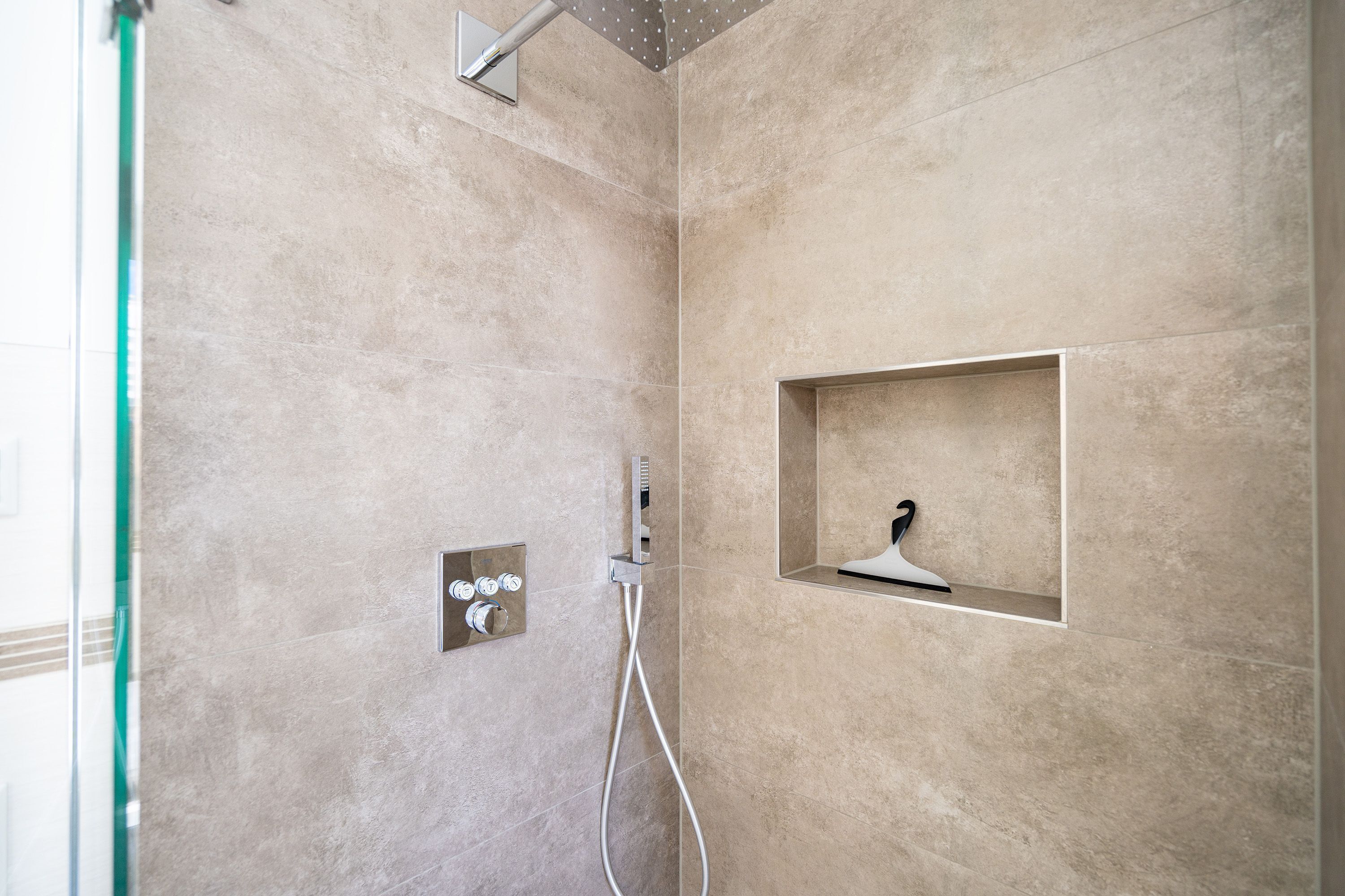 A modern shower area with beige tiles, a handheld showerhead, and a control panel with multiple buttons.