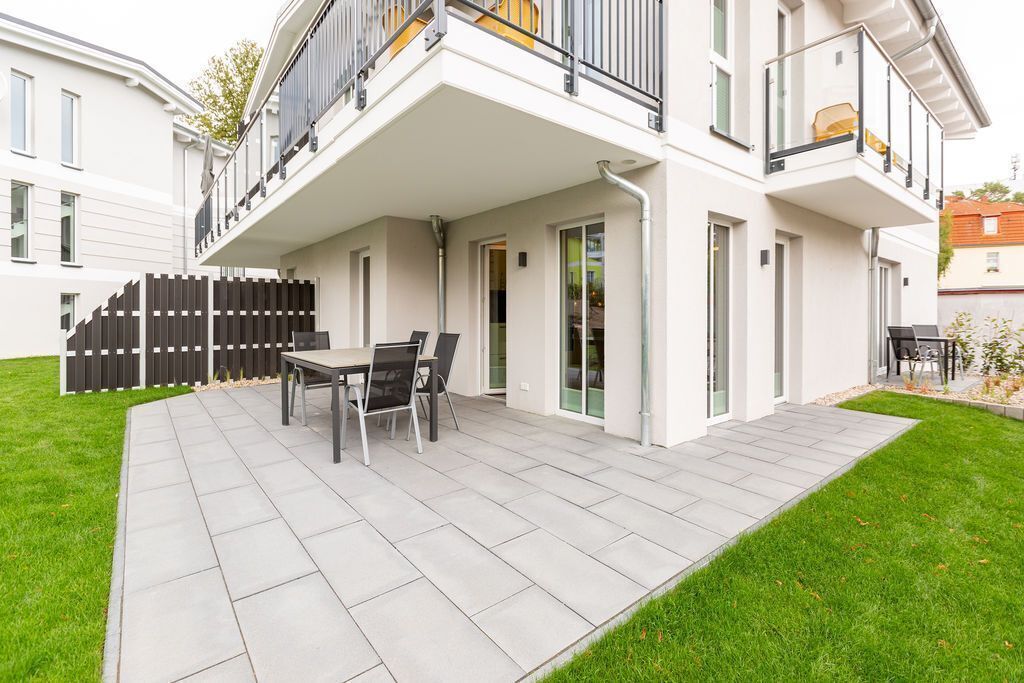 A modern two-story house with a covered patio area, a dining table, and chairs.