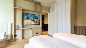 Quarto com cama, televisão presa a uma prateleira de madeira, escrivaninha e cadeira.