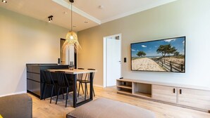 Uma sala de estar moderna com área de jantar, uma televisão de tela plana grande fixada na parede e piso de madeira.