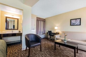 A hotel room with a bed, a desk, a chair, a sofa, a coffee table, a mirror, a window with curtains, and an air conditioning unit. - Boca Suites Deerfield Beach Surestay Collection BW (Deerfield Beach)