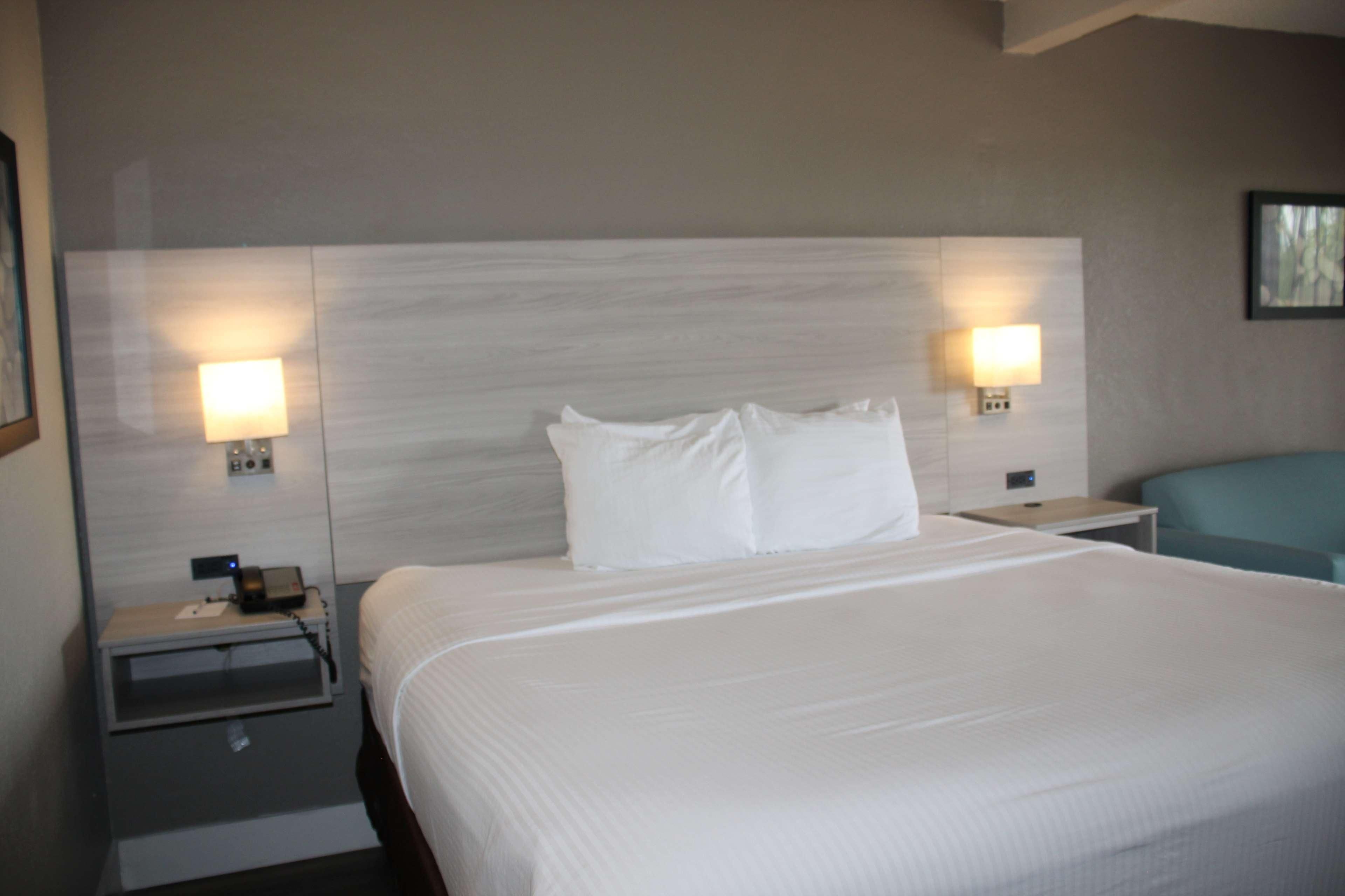 A hotel room with a large bed, two bedside tables with lamps, a nightstand, and a blue chair.