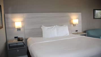 A hotel room with a large bed, two bedside tables with lamps, a nightstand, and a blue chair.