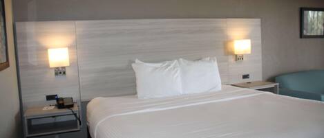 A hotel room with a large bed, two bedside tables with lamps, a nightstand, and a blue chair.
