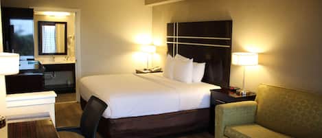 Una habitación de hotel con una cama, lámparas de noche, un escritorio, una silla y un sofá.