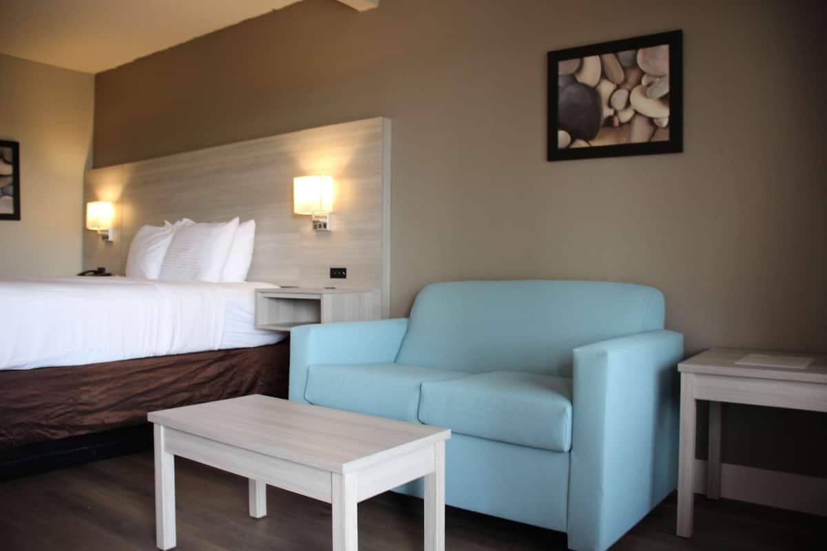 Una camera d'albergo con un letto, una poltrona azzurra, un piccolo tavolino e due lampade a parete.