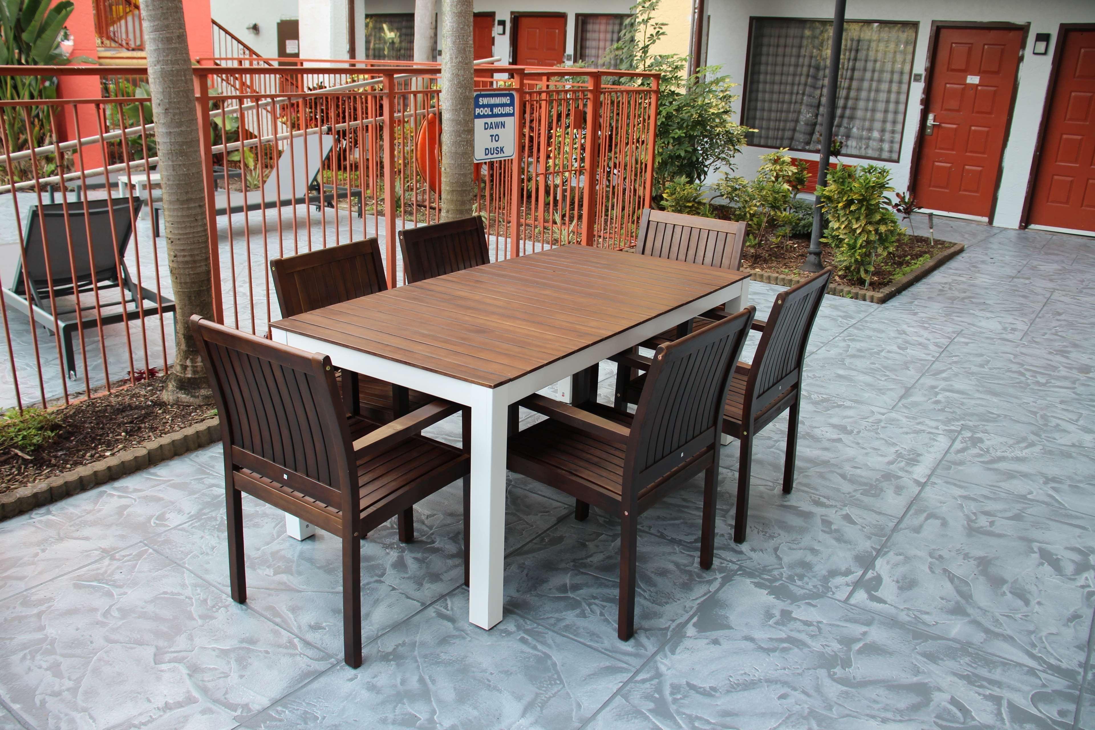 Une terrasse avec une table et des chaises en bois, une clôture en métal et un panneau indiquant les heures d’ouverture de la piscine.