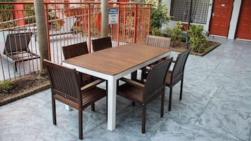 Une terrasse avec une table et des chaises en bois, une clôture en métal et un panneau indiquant les heures d’ouverture de la piscine.