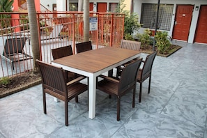 A patio with a wooden table and chairs, a metal fence, and a sign indicating pool hours. - Boca Suites Deerfield Beach Surestay Collection BW (Deerfield Beach)