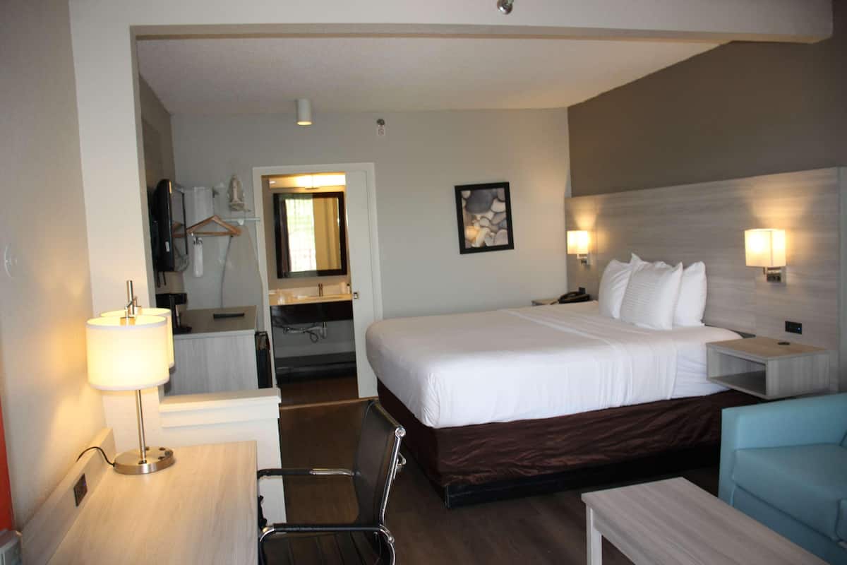 Una camera d'albergo con un letto, comodini, una scrivania, una sedia, uno specchio, un bagno e un quadro appeso al muro.