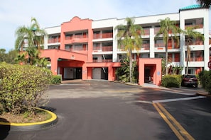 Um hotel com vários andares, fachada em vermelho e branco, diversas varandas e estacionamento.