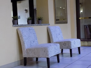 Dos sillones tapizados con tela estampada, un espejo y plantas en macetas sobre un suelo de baldosas.