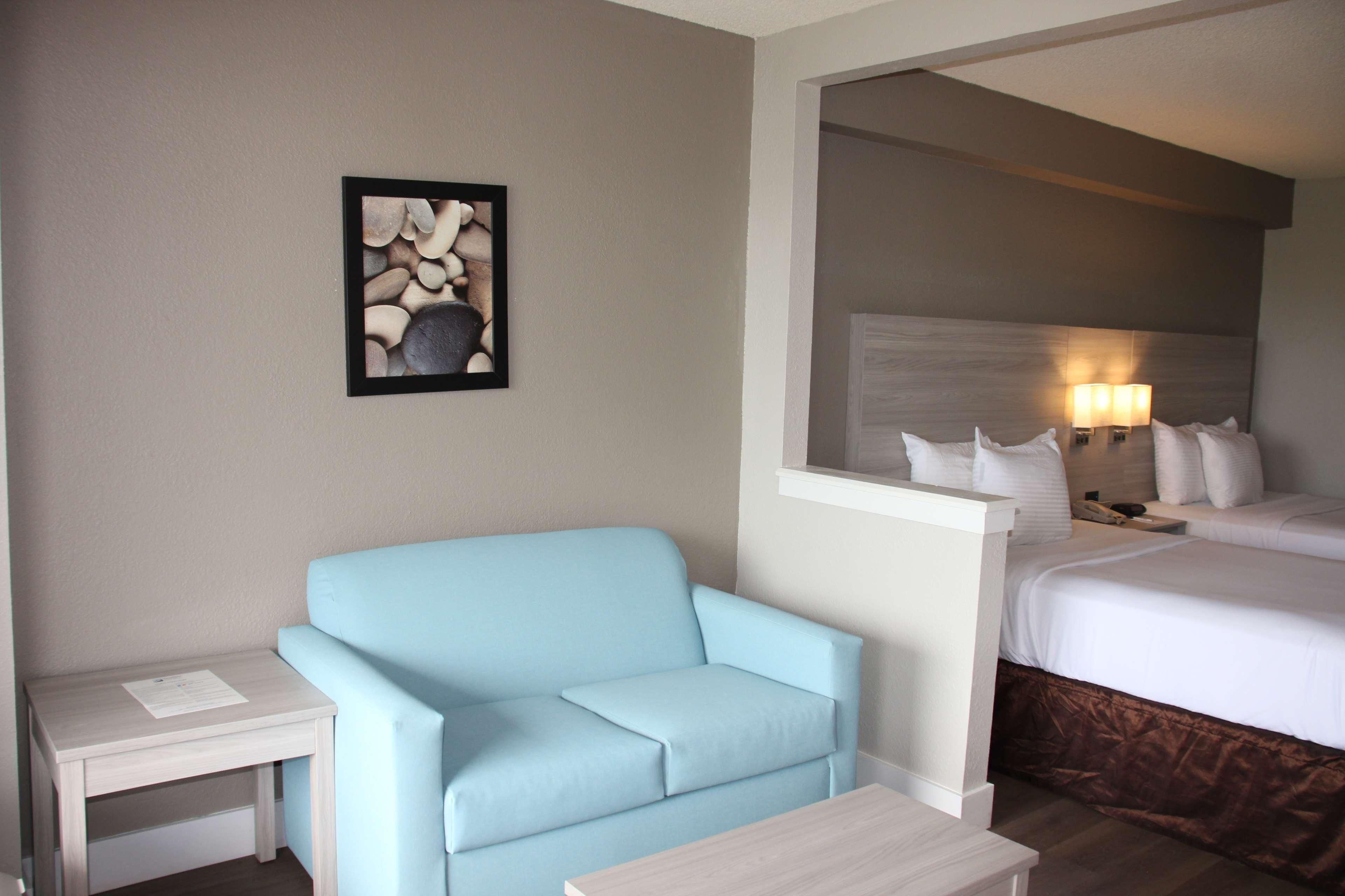 A hotel room with a light blue sofa, a small white table, a bed with white bedding, and a wall-mounted picture of stones.