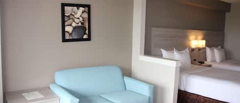 A hotel room with a light blue sofa, a small white table, a bed with white bedding, and a wall-mounted picture of stones.