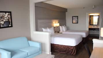 A hotel room with two beds, a light blue sofa, a small table, and a bathroom visible through an open door.