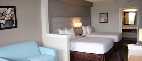 Ett hotellrum med två sängar, en ljusblå soffa, ett litet bord och ett badrum som syns genom en öppen dörr.