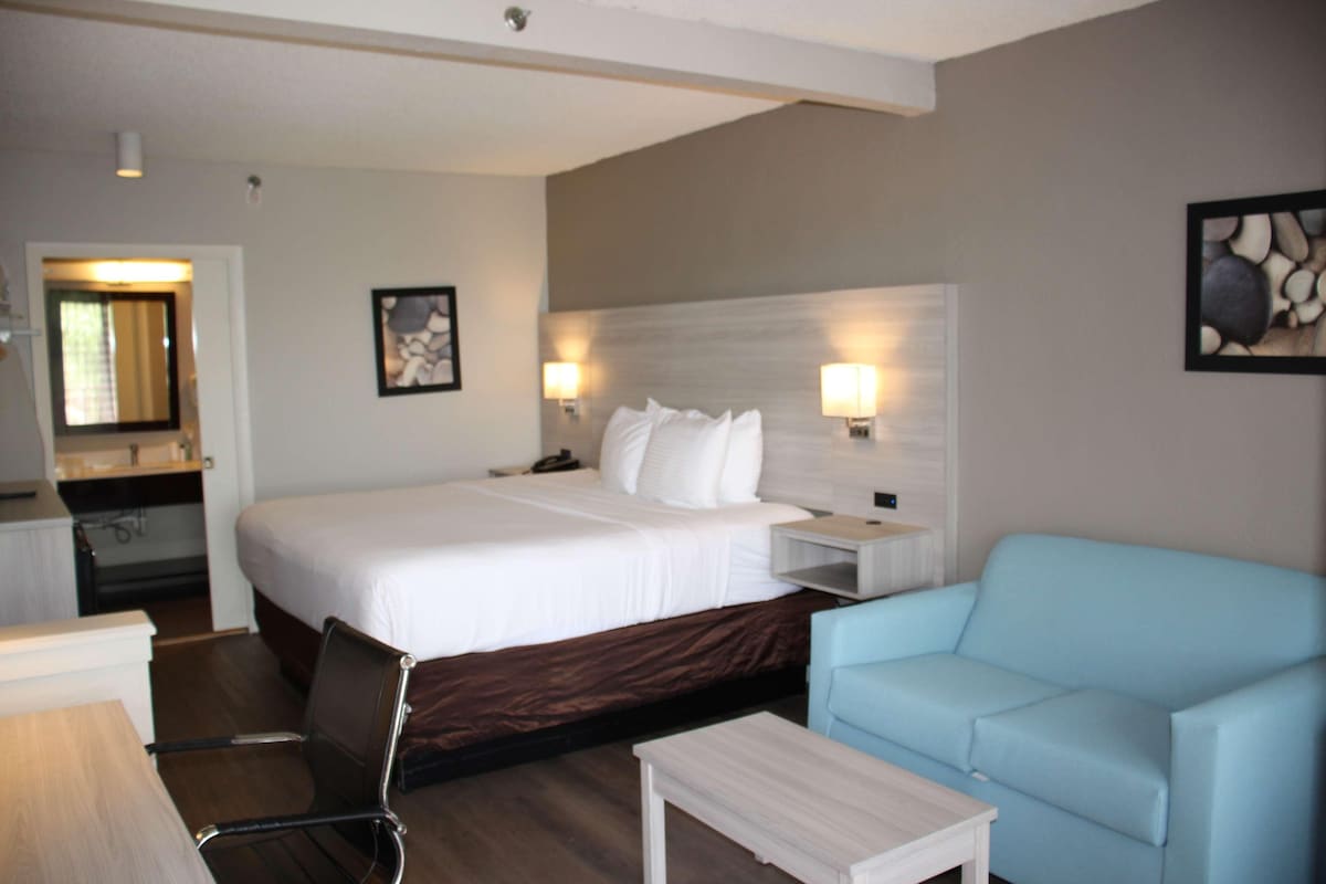 A hotel room with a bed, a desk, a chair, a sofa, and two wall-mounted lamps.