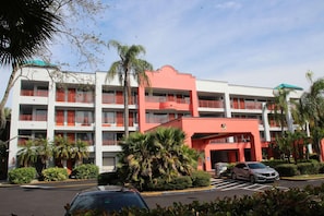 A multi-story hotel with balconies, a parking lot, and palm trees. - Boca Suites Deerfield Beach Surestay Collection BW (Deerfield Beach)
