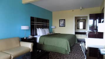 A hotel room with a bed, a desk, a chair, a sofa, a lamp, a mirror, and a television.