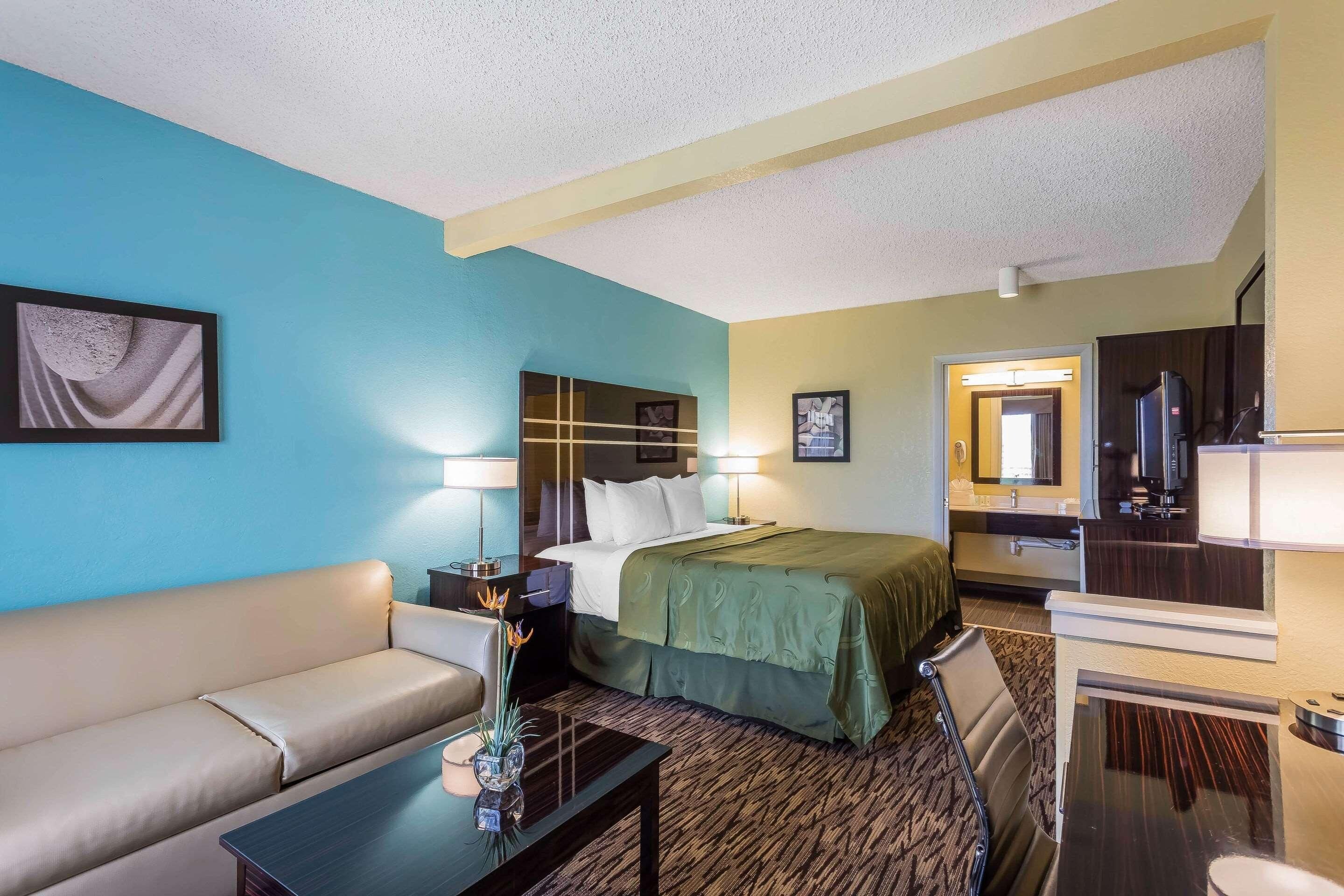 Habitación de hotel con cama, sofá, escritorio y espejo.
