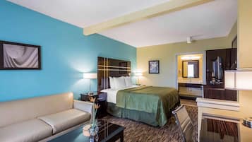 A hotel room with a bed, a sofa, a desk, and a mirror.