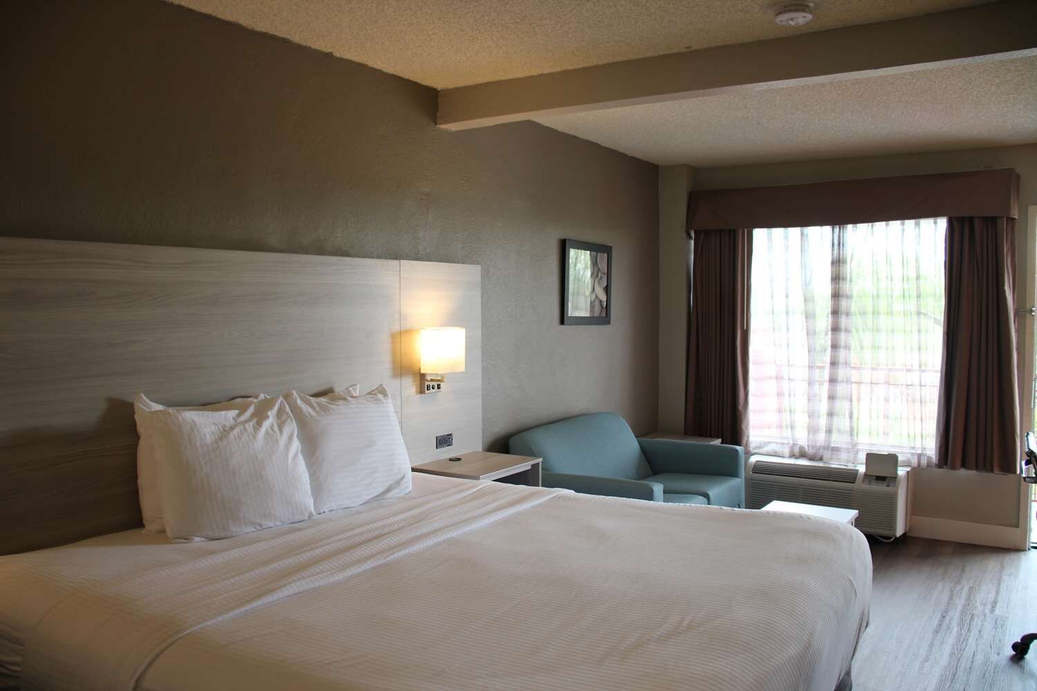 A hotel room with a large bed, a desk, a chair, and a window with curtains.