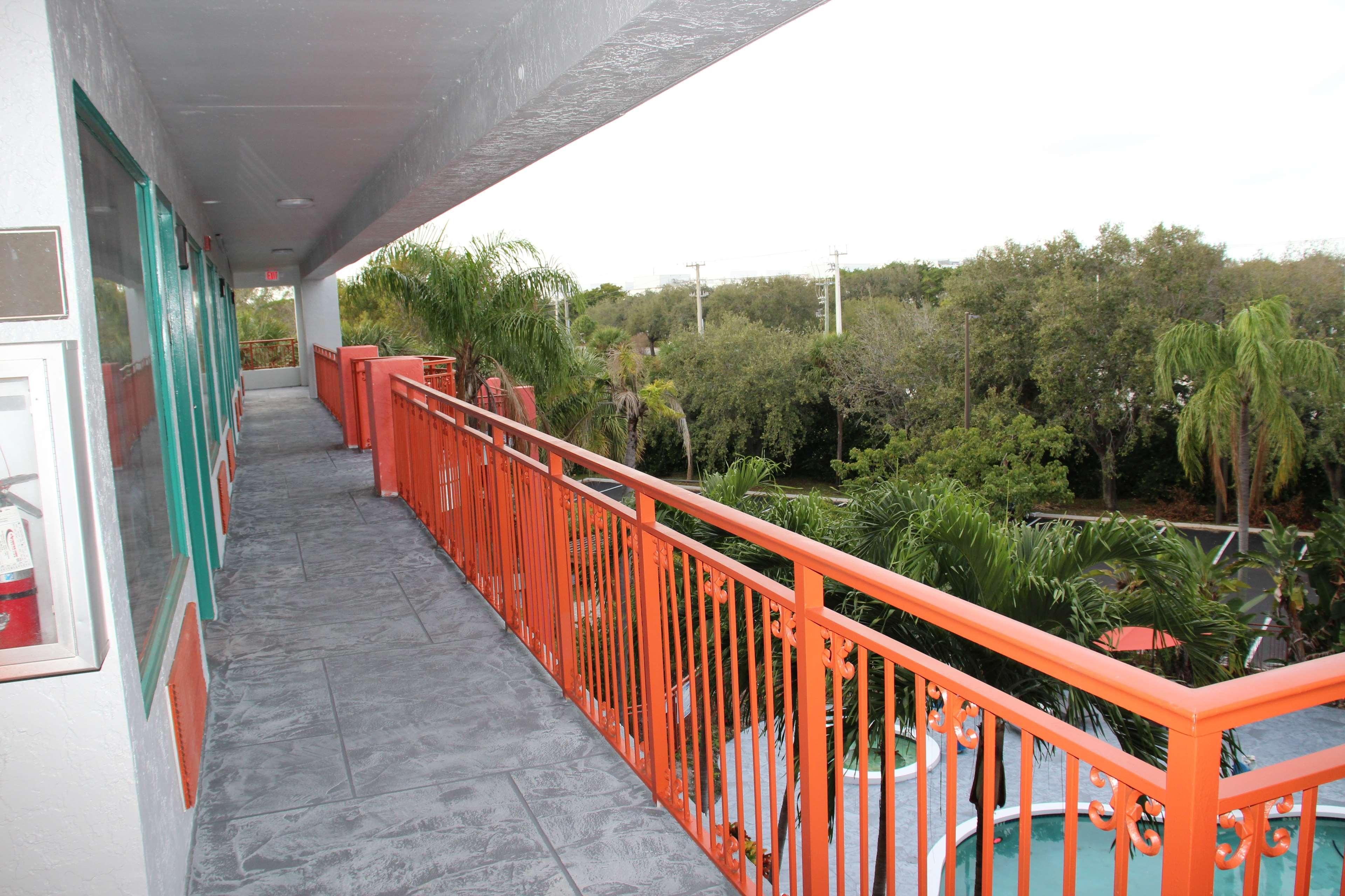 A balcony with a red railing, a tiled floor, and a view of greenery and trees.