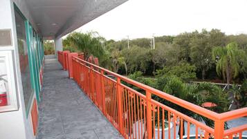 A balcony with a red railing, a tiled floor, and a view of greenery and trees.