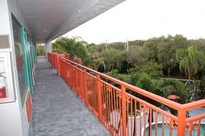 A balcony with a red railing, a tiled floor, and a view of greenery and trees.
